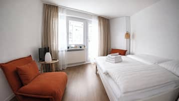 A hotel room with a bed, a chair, a TV, a small table, and a window with curtains.