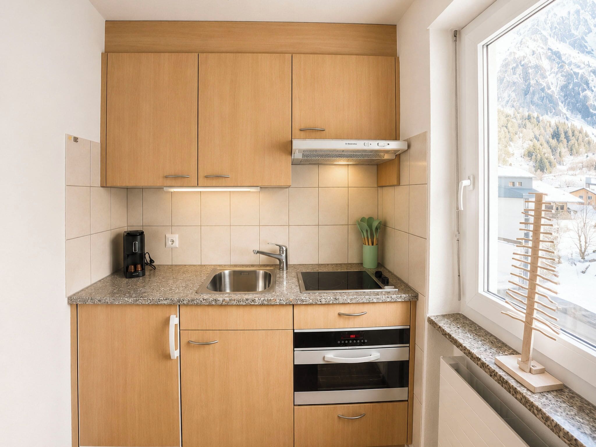 A compact kitchen with wooden cabinets, a stainless steel sink, and an oven.