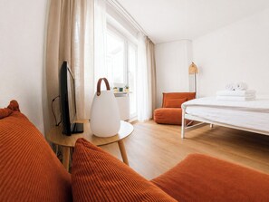 A hotel room with a bed, a desk with a lamp, a television, and orange cushions. - Majesta Leukerbad # 2-bed apartment, Dusche, WC by Interhome (Leukerbad)