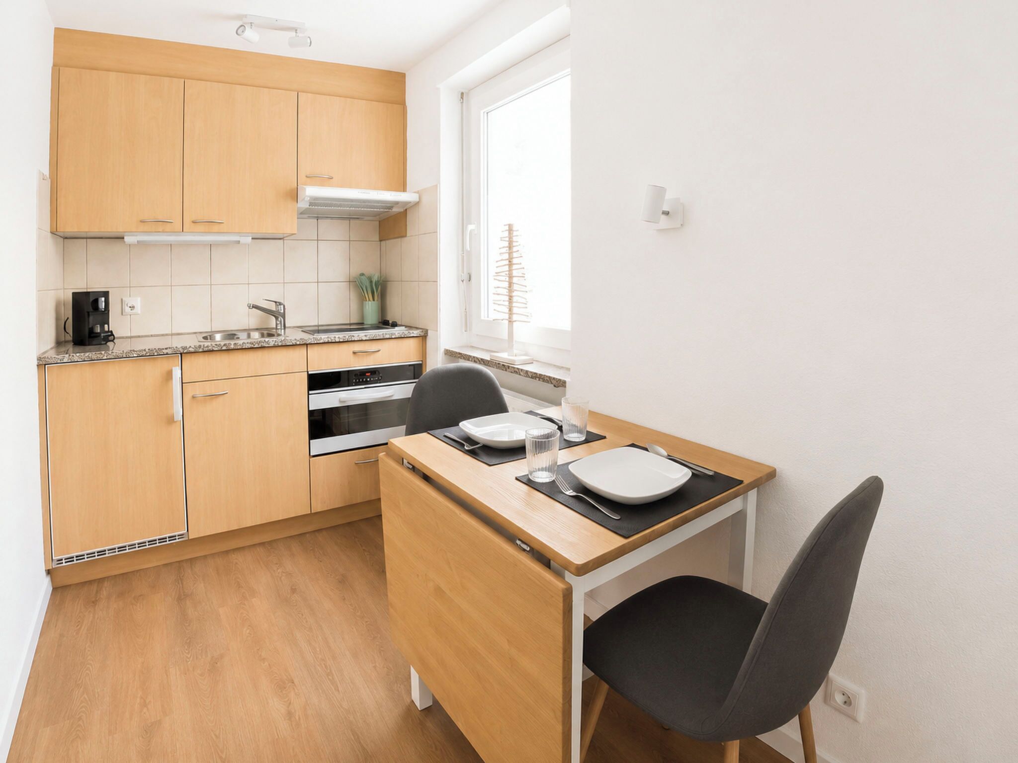 A compact kitchen with wooden cabinets, a built-in oven, and a small dining area with a table and chair.