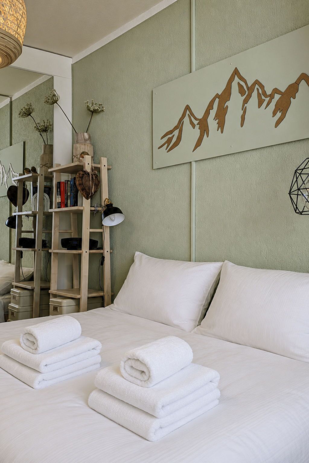 Quarto de hotel com uma cama, toalhas, uma estante e uma obra de arte na parede.
