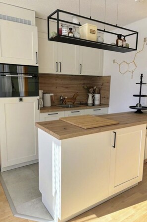 A modern kitchen with white cabinetry, a wooden countertop, and a black hanging shelf above. - Majesta Leukerbad # 2-bed apartment, Bad, WC by Interhome (Leukerbad)