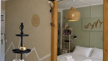 Une chambre d’hôtel avec un lit, une table en bois sur laquelle se trouvent une planche à découper et des saucisses, une étagère avec des objets décoratifs et une étagère murale avec des livres et une lampe.