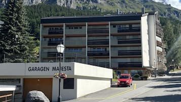 Um edifício com a placa 'GARAGEN MAISTETA', uma área de estacionamento e um carro vermelho estacionado em frente.