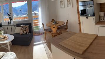 Una sala de estar acogedora con un sofá, una mesa de comedor y una zona de cocina con refrigerador y cafetera.