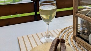Ein Glas Weißwein auf einem Holztisch, im Hintergrund eine Berglandschaft und eine Flagge.