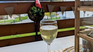 Um copo de vinho branco sobre uma mesa de madeira, com vista para montanhas e uma bandeira ao fundo.