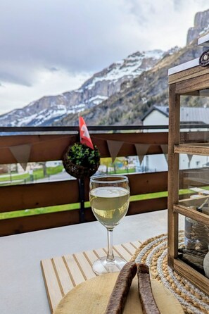 A glass of white wine on a wooden table with a view of mountains and a flag in the background. - Majesta Leukerbad # 2-bed apartment, Bad, WC by Interhome (Leukerbad)