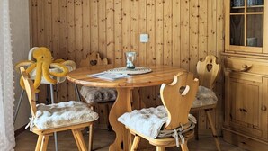 Ein Zimmer mit Holzwänden, einem runden Holztisch, vier Stühlen mit gepolsterten Sitzflächen, einer weißen Pendelleuchte und einem Schrank mit Gläsern.