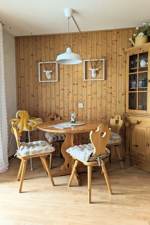 A wooden-paneled room with a round wooden table, four chairs with cushioned seats, a white pendant light, and a cabinet with glassware. - Majesta Leukerbad # 2-bed apartment, Bad, WC by Interhome (Leukerbad)