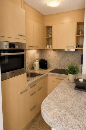 Uma cozinha compacta com forno Bosch, pia, cafeteira e uma planta em vaso.