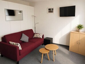 A red sofa with patterned cushions, a small wooden table, a black cabinet, and a television mounted on the wall. - Majesta Leukerbad # 3-bed apartment, Bad, WC by Interhome (Leukerbad)