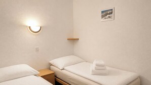 Camera d'albergo con due letti singoli, un comodino, una lampada a parete e una piccola mensola.
