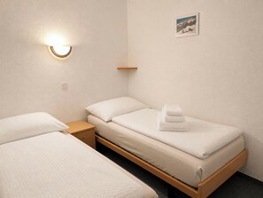 Ein Hotelzimmer mit zwei Einzelbetten, einem Nachttisch, einer Wandlampe und einem kleinen Regal.