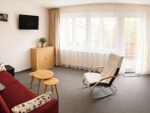 Ein modernes Wohnzimmer mit einem roten Sofa, einem weißen Schaukelstuhl, einem Holzkabinett und einem kleinen Tisch.