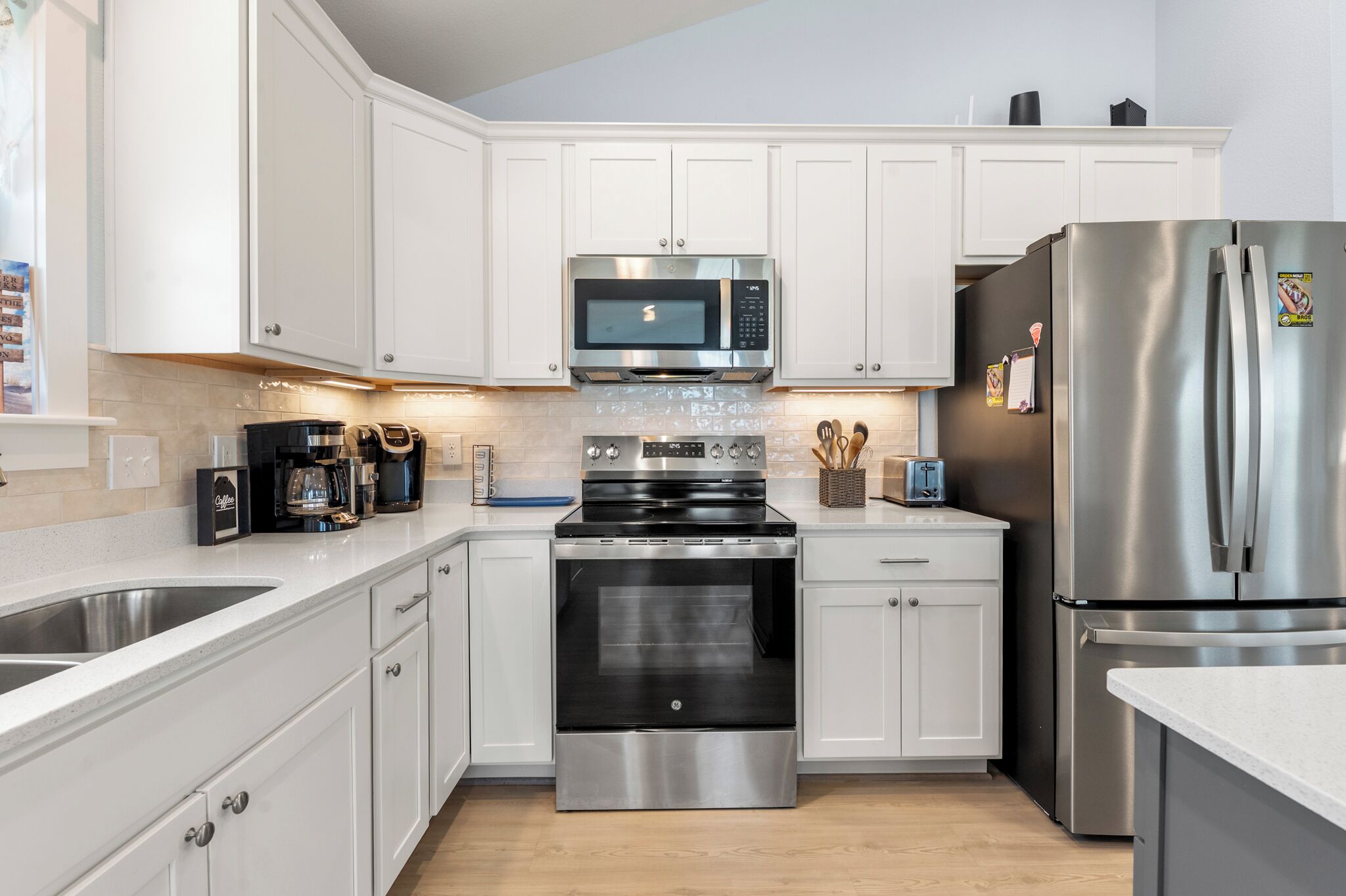 A modern kitchen with white cabinets, stainless steel appliances, a microwave, oven, and refrigerator.