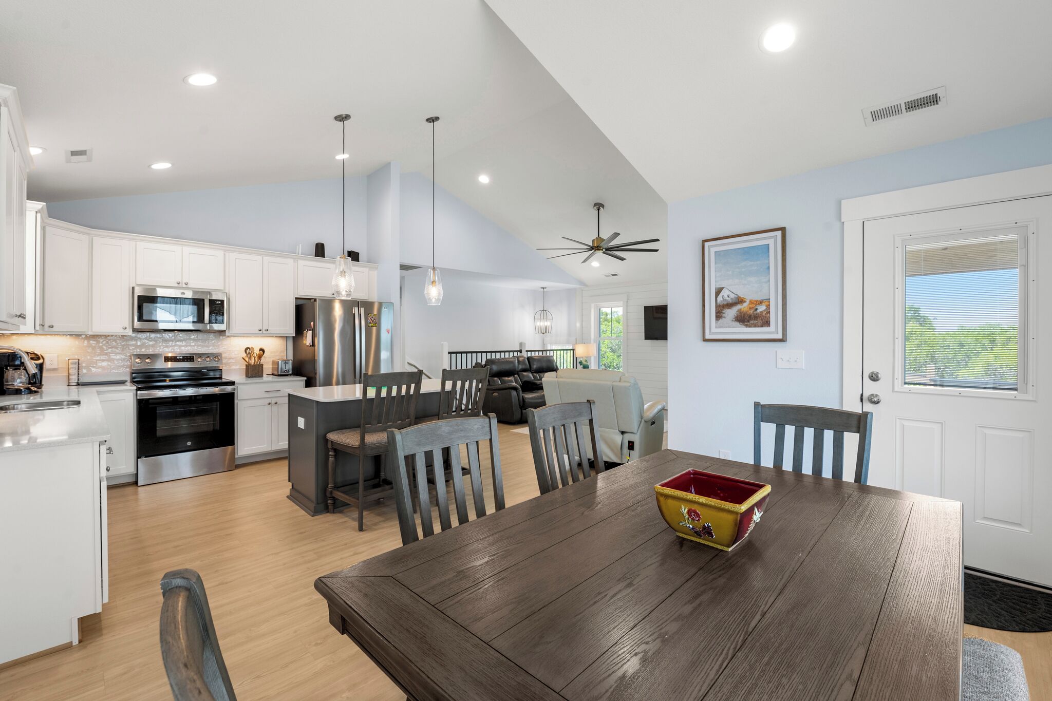 A modern kitchen with white cabinets, stainless steel appliances, and a dining area with a wooden table and chairs.