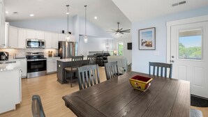 A modern kitchen with white cabinets, stainless steel appliances, and a dining area with a wooden table and chairs. - HIAV13: The Green Turtle and the Nest (Avon)