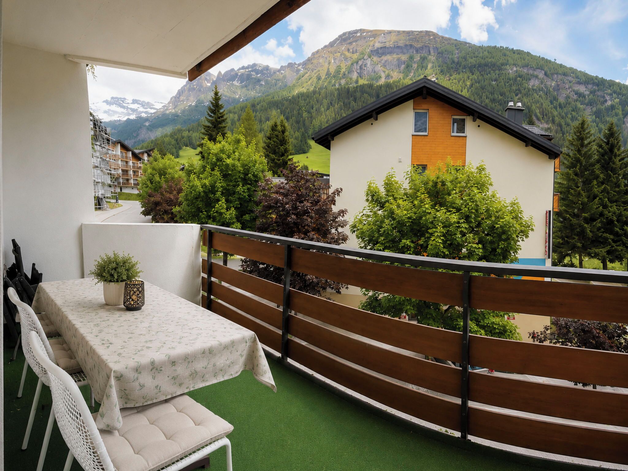 A balcony with a table and chairs, a potted plant, and a view of a mountain and buildings.