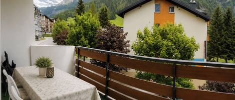 A balcony with a table and chairs, a potted plant, and a view of a mountain and buildings.
