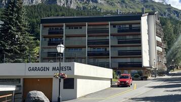 Un edificio con la inscripción 'GARAGEN MAISTETA', con una zona de estacionamiento y un coche rojo estacionado al frente.