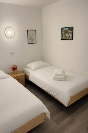 A room with two single beds, a bedside table with a lamp, and a wall-mounted light. - Majesta Leukerbad # 2-bed apartment, Bad, WC by Interhome (Leukerbad)