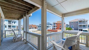 A covered porch with white railings, two Adirondack chairs, and a view of neighboring buildings. - NH3310: Chasing the Sun (Nags Head)