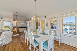 Un vaste espace dédié à la salle à manger, avec une grande table, des chaises blanches et une vue sur un immeuble par la fenêtre.