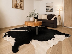 A room with a round wooden coffee table, a black and white cowhide rug, a brown sofa, a floor lamp, and a painting on the wall. - Majesta Leukerbad # 3-bed apartment, Dusche, WC by Interhome (Leukerbad)