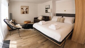 Una camera d'albergo con un letto, una sedia, un divano, una lampada e opere d'arte alle pareti.
