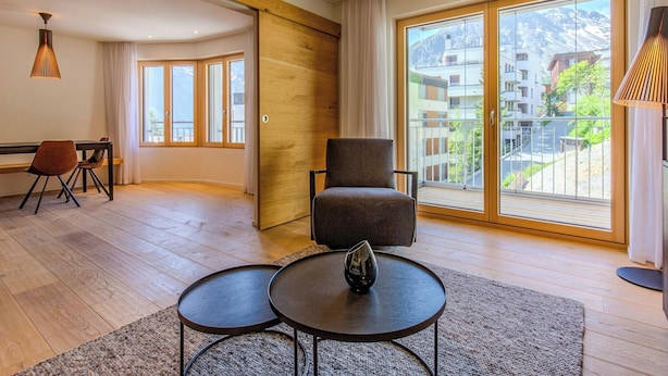Ein geräumiger Wohnbereich mit einem großen Schiebeglastür, die auf einen Balkon führt, einem Essbereich mit einer Bank und einem modernen Sessel.
