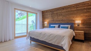 Ein Schlafzimmer mit einer Holzwand, einem großen Bett, einem Nachttisch und Blick durch eine Schiebetür.