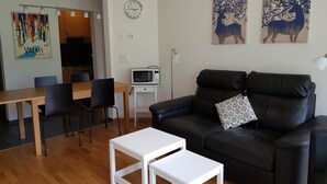 En moderne stue med en sort lædersofa, et hvidt sofabord og et spiseområde med stole og bord.