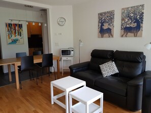Ein modernes Wohnzimmer mit einem schwarzen Ledersofa, einem weißen Couchtisch und einem Essbereich mit Stühlen und Tisch.