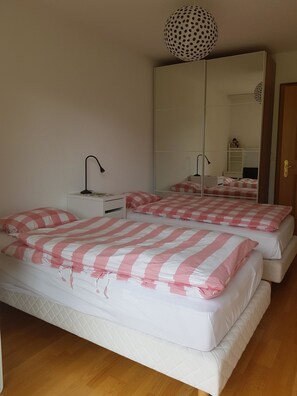 Ein Schlafzimmer mit zwei Betten, einem Nachttisch, einer Lampe, einem großen Spiegel und einer Pendelleuchte.