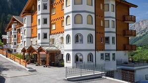 Et hotel med flere etager, en receptionsdisk, altaner og et bjergrigt landskab i baggrunden.