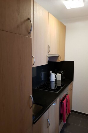 Een moderne keuken met houten kastjes, een zwart aanrecht, een waterkoker, een koffiezetapparaat en een rode handdoek aan de muur.