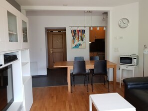 A modern kitchen with wooden cabinets, a dining table with chairs, a microwave, and a clock on the wall. - Edelweiss C 22 # 4-bed apartment, Dusche, WC 4-Bettwohnung, Dusche, WC by Interhome (Leukerbad)