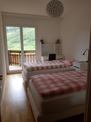 Een slaapkamer met twee bedden, een bureau en uitzicht op een groen landschap door een schuifdeur.