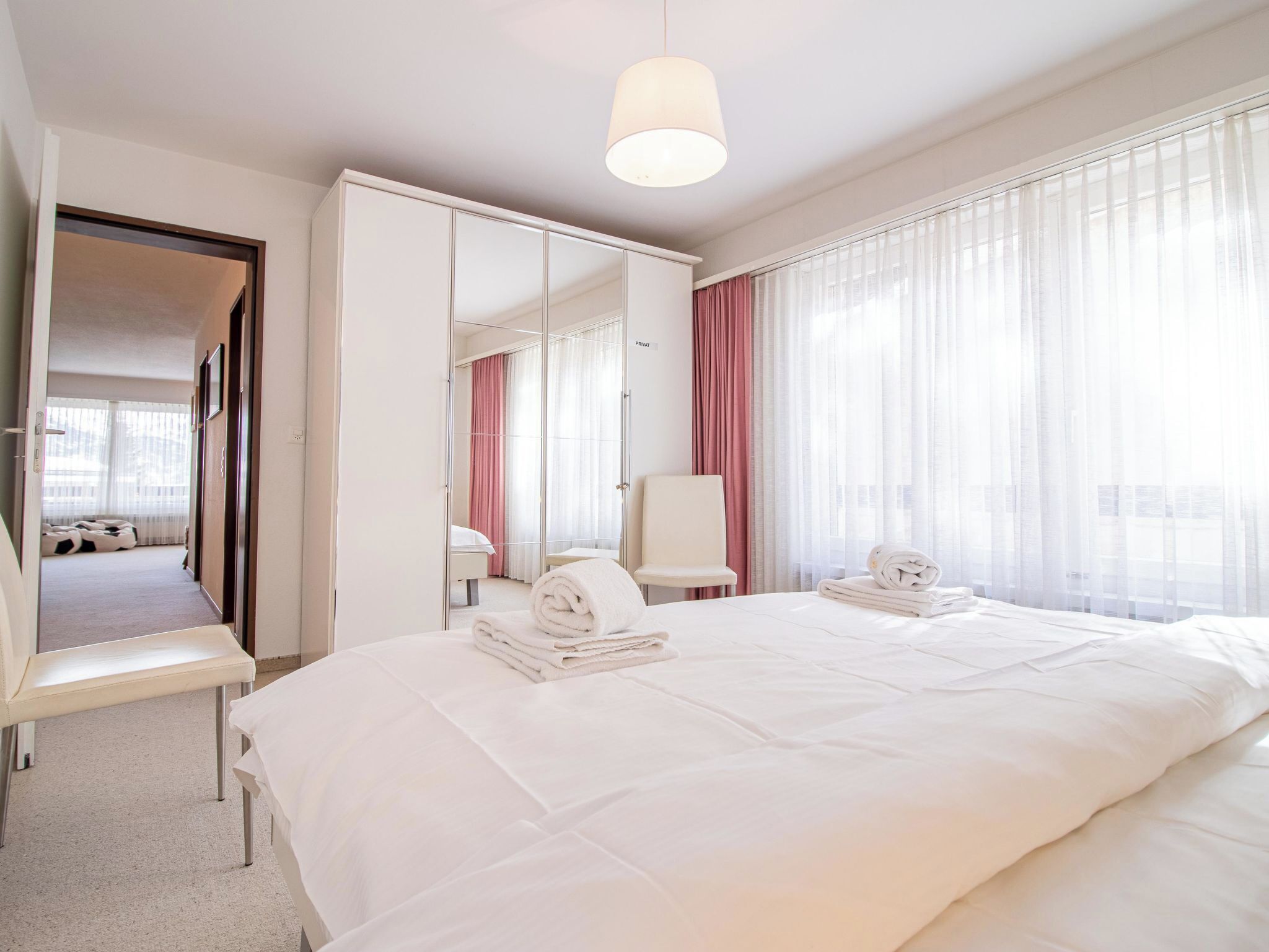 A hotel room with a large bed, a sitting area with a chair, a mirror, and a wardrobe.
