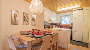 Et moderne køkken med hvide skabe, træloft og et spiseområde med et træbord og stole.