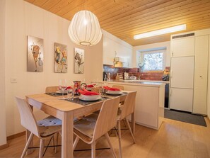 Eine moderne Küche mit weißen Schränken, einer Holzbalkendecke und einem Essbereich mit einem Holztisch und Stühlen.