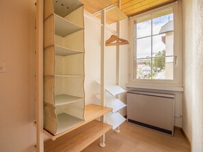 Une pièce avec un banc en bois, une étagère à rayures et une fenêtre donnant sur des immeubles et une montagne.