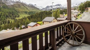 En balkon med trægelænder, der udover et bjerglandskab med huse og en vej.