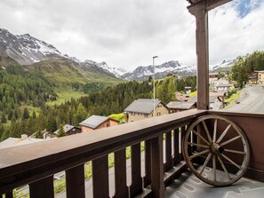 Ein Balkon mit Holzwertung, der auf eine Berglandschaft mit Häusern und einer Straße blickt.