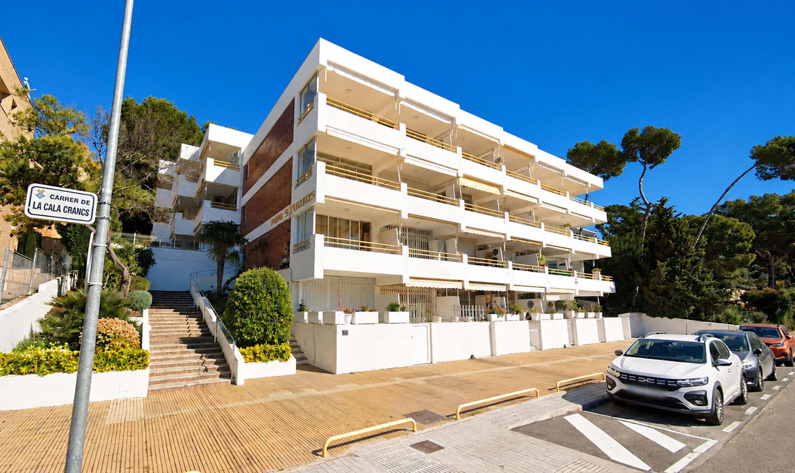 A multi-story building with balconies, a staircase, and a sign indicating 'Carrer de la Cala Crances.'