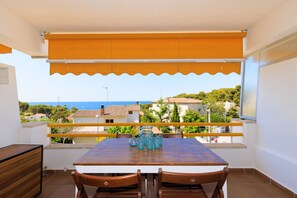 Ein Balkon mit Tisch und Stühlen, Blick auf das Meer, und ein Gebäude im Hintergrund.