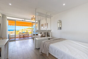 Ein Schlafzimmer mit Bett, Schreibtisch, Stuhl, einem Balkon mit Aussicht und einer Hängeleuchte.