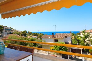 Ein Balkon mit gelb gestrichenem Geländer, einem Tisch und einer blauen Glasflasche.