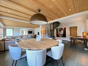 Un espacio habitable moderno con una mesa redonda de madera rodeada de sillas, un sofá y una escalera.